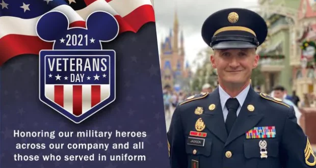 A proud veteran in uniform stands beside the vibrant 2021 Veterans Day Disney sign, celebrating military heroes and Disney Cast Members who serve, creating a special moment of tribute within the magic of the park.