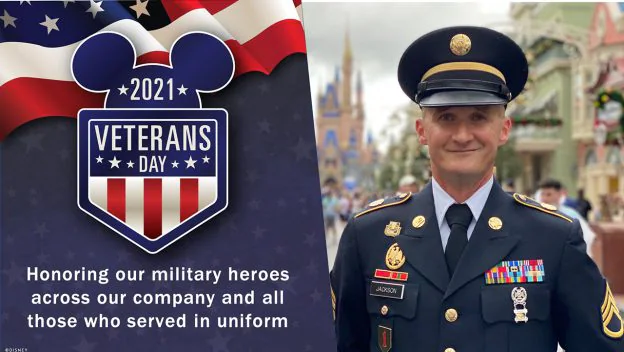 A proud veteran in uniform stands beside the vibrant 2021 Veterans Day Disney sign, celebrating military heroes and Disney Cast Members who serve, creating a special moment of tribute within the magic of the park.
