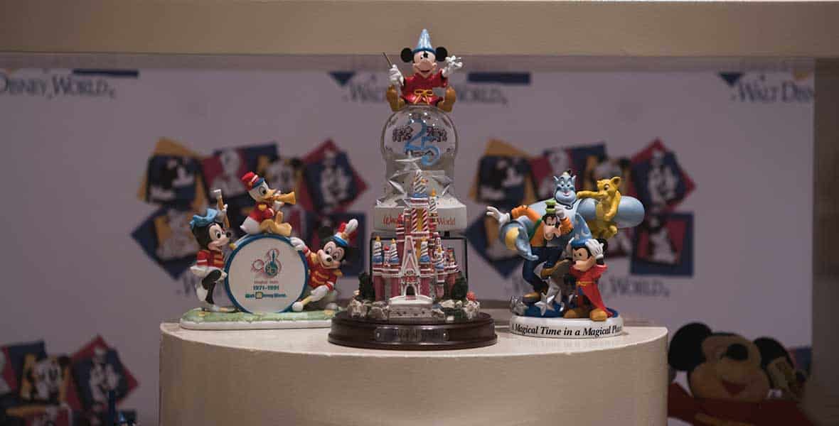 Mickey Mouse, Genie, and other beloved Disney characters as collectible figurines showcased on circular stands inside a themed display setting.