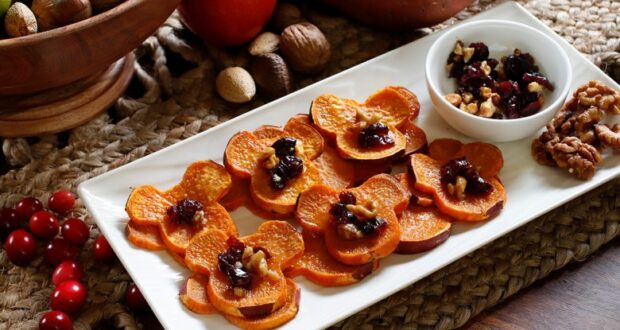 Sliced sweet potatoes topped with cranberries and nuts are presented on a cheerful white platter—this colorful snack brings festive flair to theme park celebrations, making it a popular treat during Kwanzaa festivities or special events at entertainment resorts.