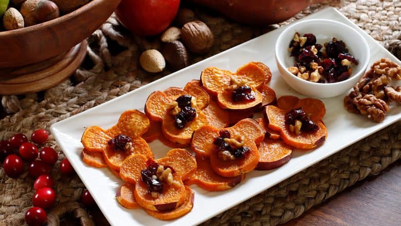 Sliced sweet potatoes topped with cranberries and nuts are presented on a cheerful white platter—this colorful snack brings festive flair to theme park celebrations, making it a popular treat during Kwanzaa festivities or special events at entertainment resorts.
