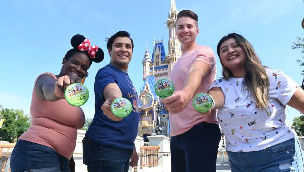 A group of excited adults proudly display green Disney celebration buttons in front of the iconic Cinderella Castle at Disney World, soaking up the enchantment and vibrant energy that makes a grown-up trip to the park unforgettable.