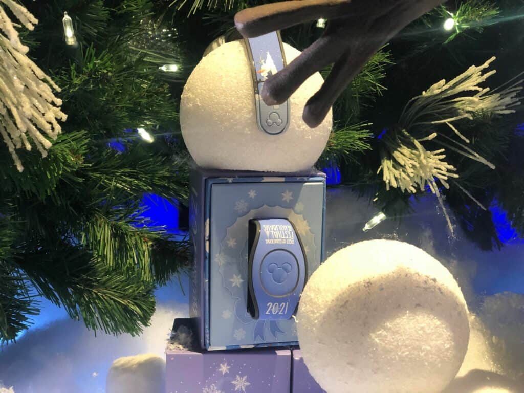 The 2021 Disney MagicBand sits nestled among festive snowballs and decorated tree branches, celebrating the holiday magic of EPCOT’s International Festival of the Holidays—a must-have collectible for any Disney Parks fan.