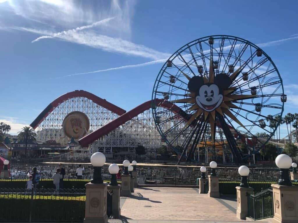 The iconic Mickey Mouse Ferris wheel and thrilling roller coaster at Disneyland California shine under a brilliant blue sky, inviting guests to make the most of their day with Disney Genie+.