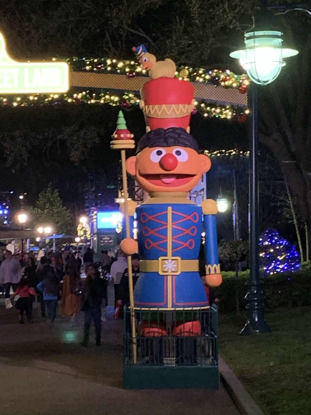Ernie the Nutcracker stands tall with his playful rubber ducky hat in a brightly decorated, festive outdoor area at night, capturing the whimsical spirit of Disney World’s New Year’s Eve holiday displays.