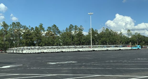 Disney World trams line up in the sprawling parking lot, ready to whisk excited guests off to the magic of the parks beneath a bright blue sky.
