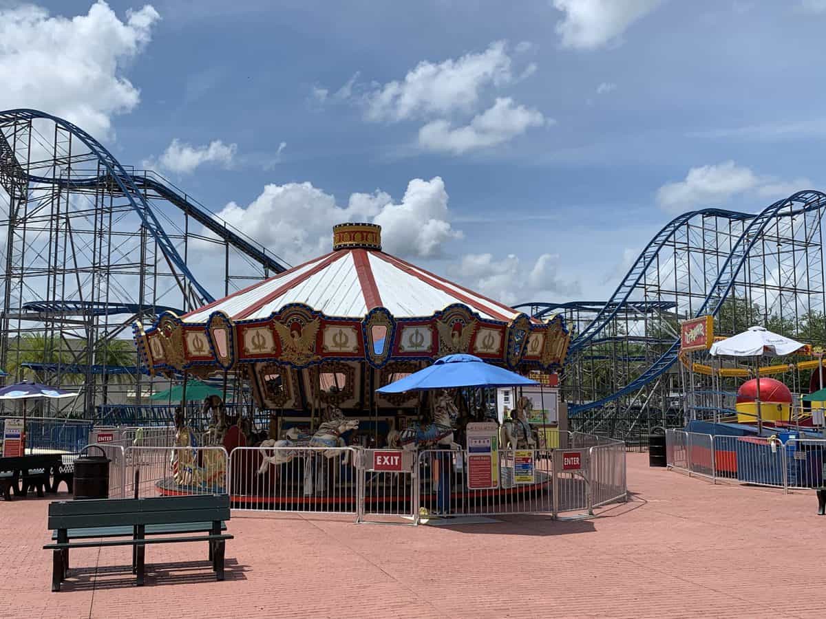 The classic Old Town amusement park comes alive with its iconic carousel and thrilling roller coaster, creating an electrifying atmosphere under a bright blue sky dotted with fluffy clouds.