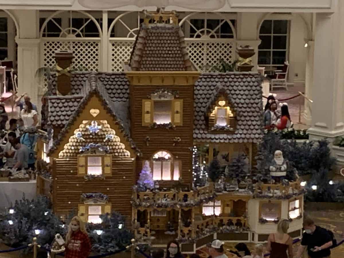 A dazzling gingerbread house illuminated with twinkling lights takes center stage indoors at Disney’s Animal Kingdom Lodge, delighting guests who gather to admire the festive holiday centerpiece in true Disney style.