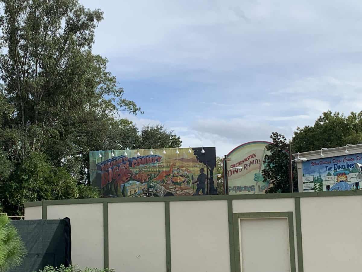 Colorful new signs and themed construction walls at DinoLand U.S.A. in Disney's Animal Kingdom, showcasing the latest updates to the area, with lush trees and blue sky visible behind.