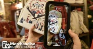 A guest at Disney World scans a Mickey Mouse-themed backpack with their phone for mobile merchandise checkout inside a park store.