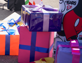 A vibrant display of gift boxes wrapped with festive ribbons in purple, pink, and orange hues, plus a box featuring playful Disney character graphics—capturing the magical spirit of giving at Disney Parks during the Ultimate Toy Drive.