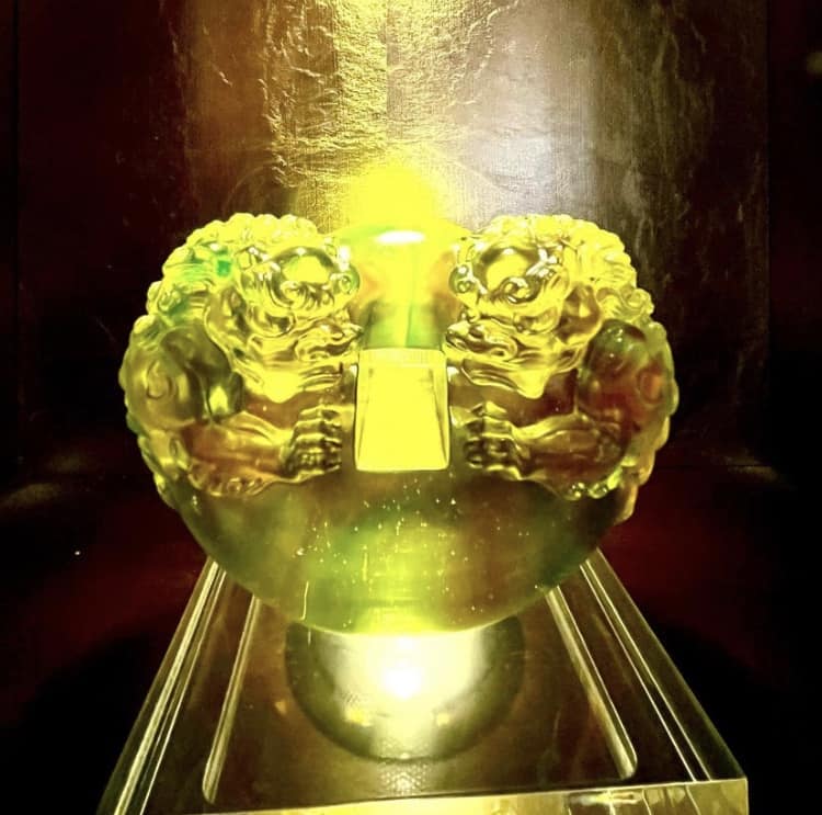 Radiant yellow-green glass orb featuring two majestic lion-like figures facing each other, perched on a crystal-clear stand—evoking the iconic decorative touches found at Nine Dragons Restaurant in EPCOT’s China Pavilion.