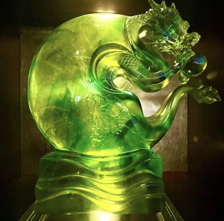A shimmering green dragon sculpture catches the glow of soft lighting as it stands proudly on a reflective surface, capturing the magic and immersive charm you’d expect from centerpiece décor at Nine Dragons Restaurant in EPCOT’s World Showcase.
