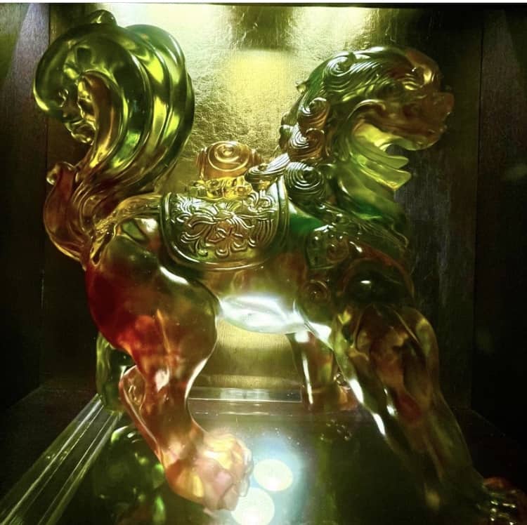 A dazzling multicolored glass lion statue with an ornate saddle shines under vivid lighting, displayed on a glossy surface—this eye-catching centerpiece captures the magical, immersive atmosphere guests love at Nine Dragons Restaurant in EPCOT’s World Showcase.