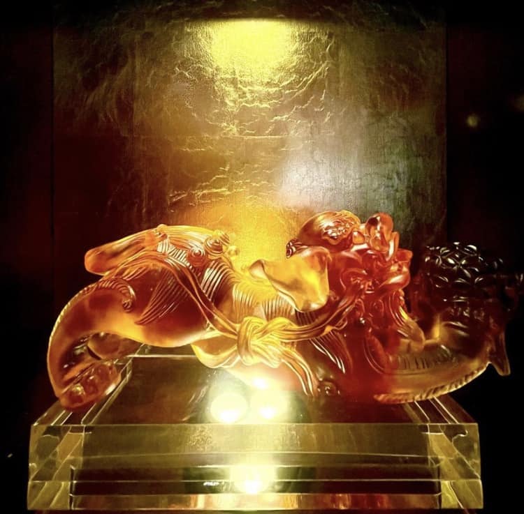 The amber dragon sculpture shines under golden lighting on a clear pedestal, standing out vividly against the dark backdrop—an eye-catching showpiece inspired by the legendary artistry of Nine Dragons Restaurant at EPCOT.