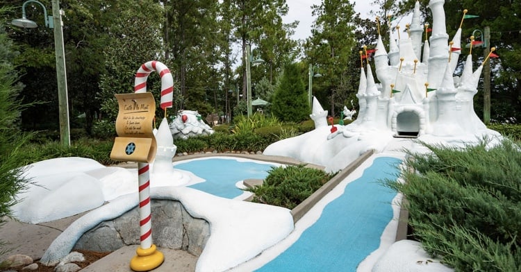 Winter-themed mini-golf course featuring a snowy castle centerpiece, winding blue stream, playful candy cane signage, and lush trees in the background. This imaginative attraction offers a fun-filled experience for families and serves as an engaging alternative to Disney parks when Disney water parks are closed.