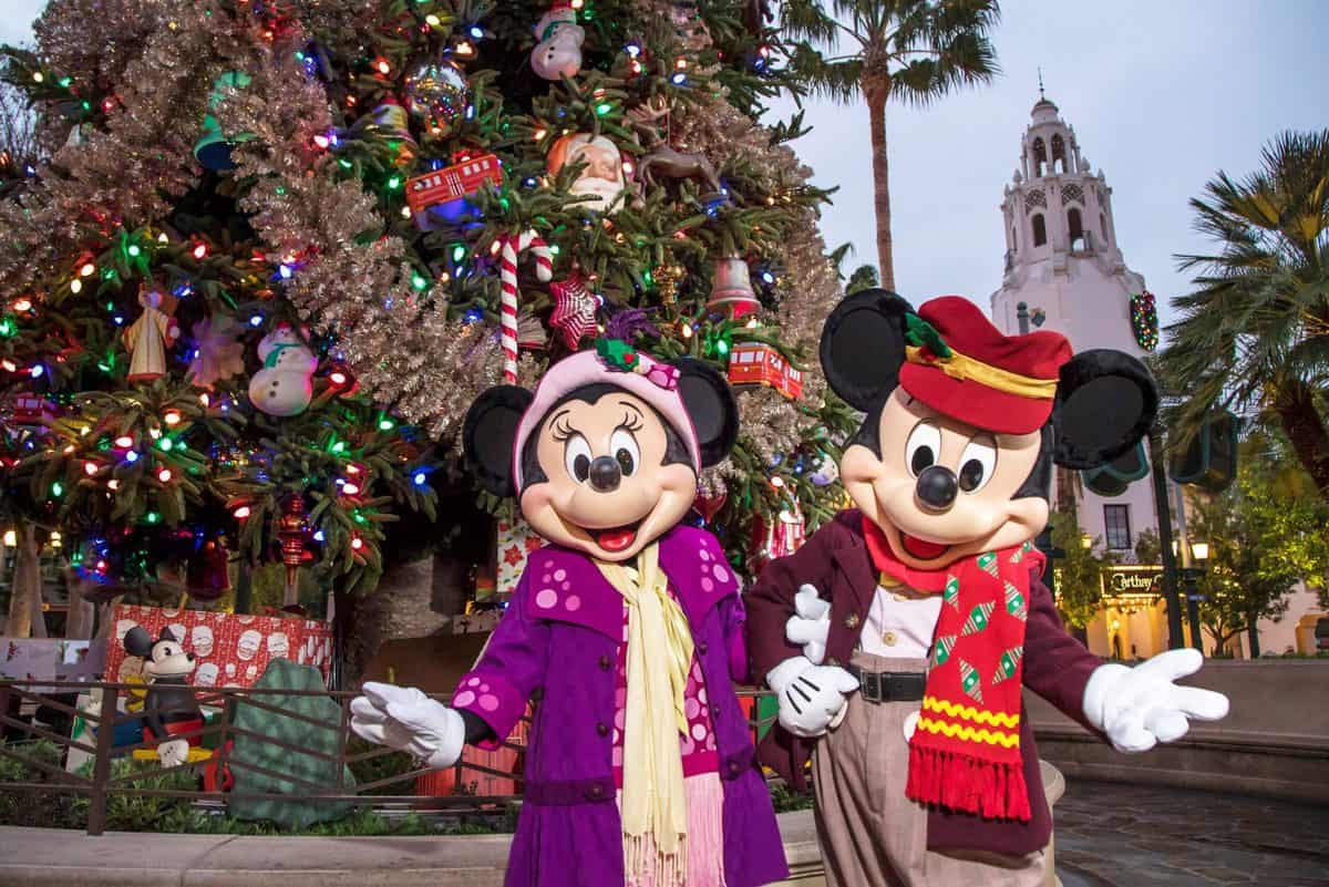 Mickey and Minnie Mouse, dressed in their festive holiday best, strike a cheerful pose in front of a beautifully decorated Christmas tree at Disney World, inviting guests to join in the seasonal magic.