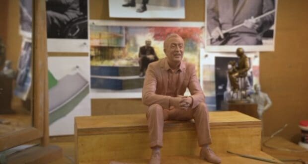 A miniature statue of Walt Disney sits on a wooden base, surrounded by vibrant photos and artwork that celebrate Disney’s legacy.
