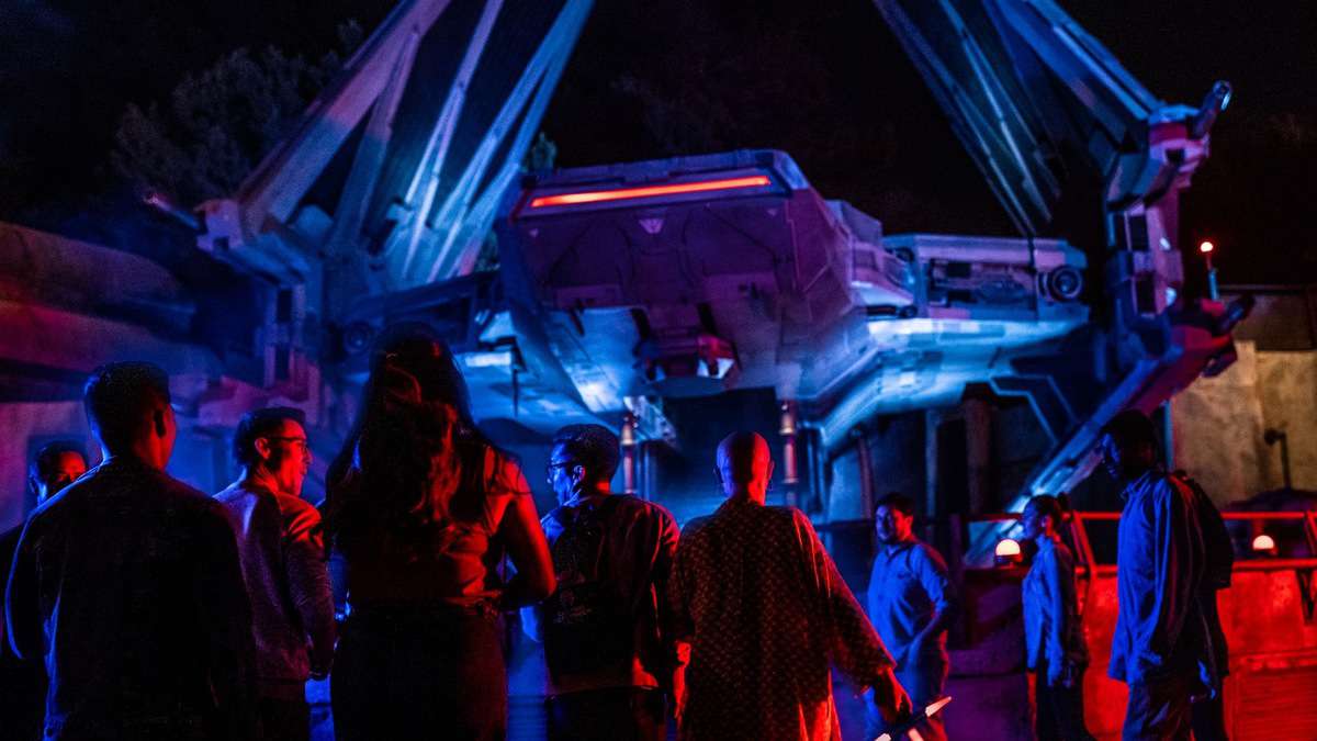 Guests gather beneath vibrant nighttime lighting beside a sleek, Star Wars-inspired spaceship at Disneyland After Dark: Star Wars Nite, capturing the electric atmosphere and immersive experience of the event.