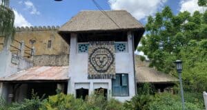 Thatched-roof building featuring a vibrant Lion King mural, surrounded by lush tropical landscaping and set against a backdrop of clear blue skies at Disney’s Animal Kingdom, capturing the immersive atmosphere of the park uninterrupted by weather concerns.