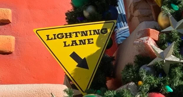 The yellow "Lightning Lane" sign with a bold black arrow pops amid festive Christmas decorations and sparkling ornaments at Disneyland California—highlighting Disney Genie+ as your ticket to holiday magic during the busy season.
