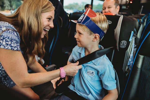 A woman helps her young son get settled into his car seat on the airport shuttle, both grinning with anticipation as they get ready to start their magical adventure to Walt Disney World near Orlando International Airport.