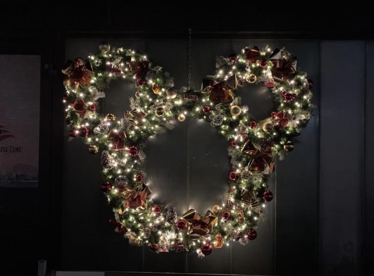 A Mickey Mouse-shaped Christmas wreath, inspired by the enchanting holiday decorations aboard the Disney Wish, sparkles with ornaments and twinkling lights—capturing the festive Disney magic fans love at theme parks and on Disney cruises.