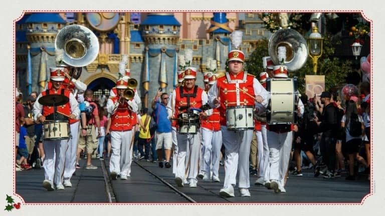 The Main Street Philharmonic in bright red uniforms performs lively tunes as they march down Main Street, U.S.A., with Cinderella Castle and cheering guests filling the background at Magic Kingdom.