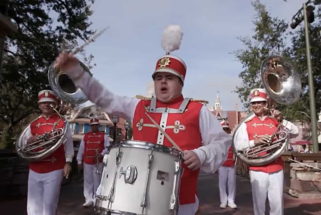 A lively marching band in bright red uniforms energizes the park, led by a spirited drummer as sousaphones shine behind them; the whole scene captures the enchanting parade atmosphere that makes Disney World so unforgettable for guests.