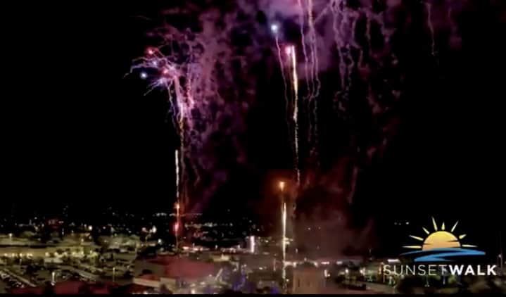 Brilliant purple fireworks dazzle above the lively park skyline, igniting excitement for a Rocking New Year celebration at Sunset Walk, with the iconic Sunset Walk logo glowing in the corner.