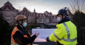 Cast Members in high-visibility vests and hard hats examine blueprints outside the Disneyland Hotel Paris at sunset, gearing up for the much-anticipated Royal Makeover of this iconic Disney landmark.