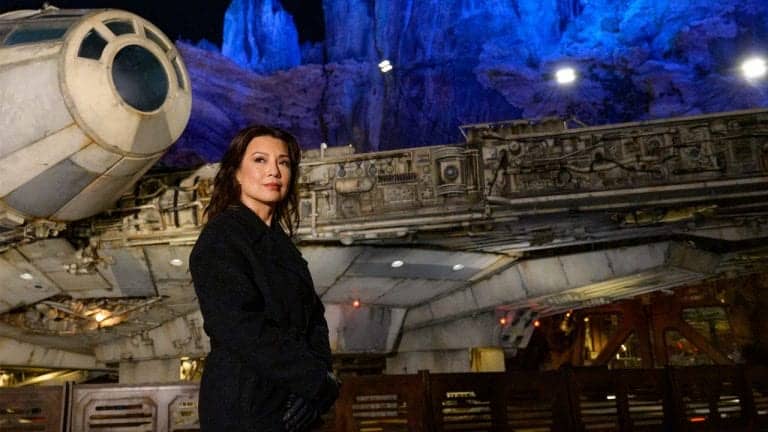 Ming-Na Wen, dressed in black, poses in front of a Star Wars spaceship set with dramatic blue-lit rocky cliffs behind her, capturing the cinematic magic of Disneyland's Galaxy’s Edge.
