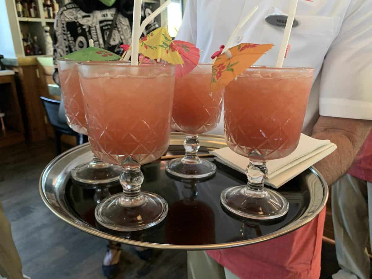 At Four Flamingos: A Richard Blais Florida Kitchen, a tray topped with four vibrant tropical cocktails—each in a glass goblet adorned with bright umbrellas and whimsical straws—captures the festive flavors and playful spirit found throughout Orlando’s favorite entertainment destinations.