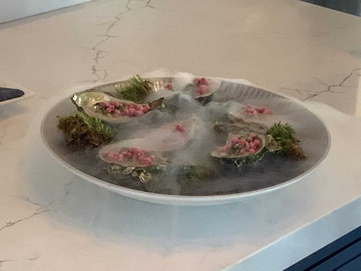 Oysters arranged on a plate with vibrant pink garnish and a dramatic smoke effect, presented atop a marble countertop—an eye-catching culinary display reminiscent of the creative dining experiences found at Universal Orlando’s themed resort restaurants.