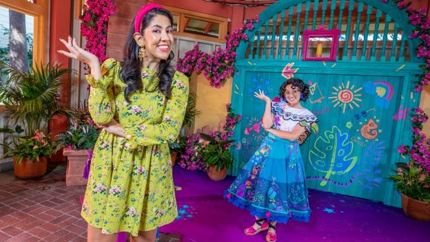 Guests enjoy a photo op amid vibrant floral displays and festive decorations at Disney California Adventure, capturing the enchanting spirit of Encanto with a touch inspired by Mirabel and Stephanie Beatriz.