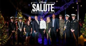 Disney veterans and military personnel gather beneath the glowing "Disney Salute" sign, surrounded by dazzling holiday lights, to celebrate during Night of a Million Lights at Give Kids The World Village.