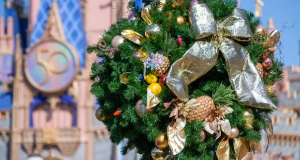 Festive holiday wreath adorned with gold ribbon and sparkling ornaments graces the foreground of Cinderella Castle at Walt Disney World, which features a prominent "50" anniversary emblem, celebrating the magical spirit of the park’s milestone season.