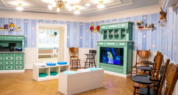 Fun-filled kids’ lounge decked out with blue wallpaper, playful green cabinets, and comfy wooden chairs, where little ones can catch their favorite cartoons on TV—an ideal retreat for young theme park guests to recharge between adventures.