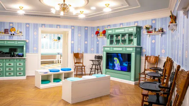 Fun-filled kids’ lounge decked out with blue wallpaper, playful green cabinets, and comfy wooden chairs, where little ones can catch their favorite cartoons on TV—an ideal retreat for young theme park guests to recharge between adventures.