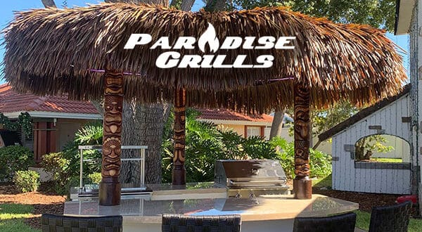 Tiki hut grill station featuring the bold "Paradise Grills" logo, nestled among lush trees and vibrant patio furniture—like stepping into a tropical theme park oasis, perfect for bringing island-inspired entertainment and festive gathering vibes to any event.