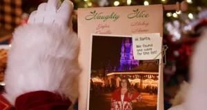 Santa presents his "Naughty List" scroll featuring a photo of a guest enjoying the dazzling holiday lights at Disneyland, highlighting the unforgettable Disney Parks seasonal photo experience.