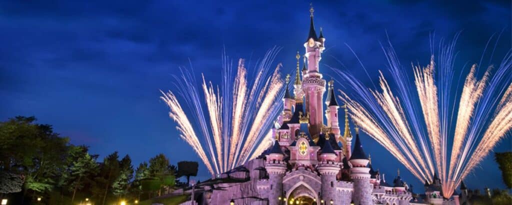 Sleeping Beauty Castle at Disneyland Paris glowing under the night sky as an incredible fireworks spectacular lights up both sides, creating a magical atmosphere for guests.