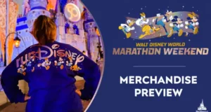 RunDisney fan in front of Cinderella Castle sporting event gear, with Disney Marathon Weekend signage and a sneak peek at 2022 marathon merchandise.