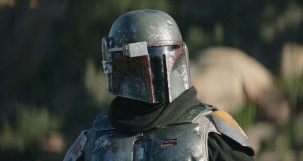 The Mandalorian in signature weathered armor and helmet poses outdoors with scenic rocky landscapes softly blurred behind him, capturing the adventure of Galaxy’s Edge.