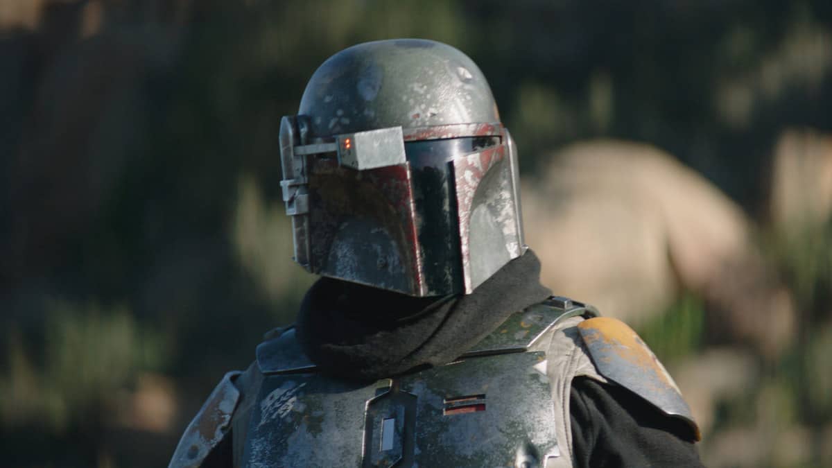 The Mandalorian in signature weathered armor and helmet poses outdoors with scenic rocky landscapes softly blurred behind him, capturing the adventure of Galaxy’s Edge.