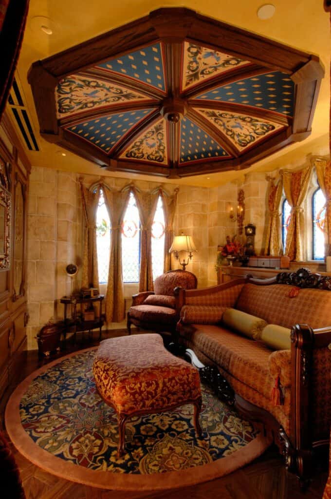 Sumptuous room featuring an ornate ceiling, plush seating, a round rug, soaring curtains, and golden lighting—evoking the magical luxury of Disney’s Cinderella Castle Suite for fans seeking that fairytale park experience.
