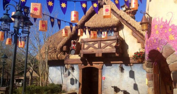 Tangled-inspired cottage at Disney World, featuring glowing lanterns, purple sunburst banners, and a charming thatched roof beneath a blue sky—this whimsical restroom area pays homage to Rapunzel’s tower and is renowned for its magical, storybook design.