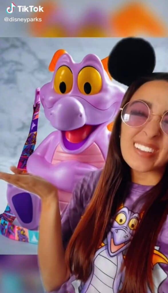 Figment fans at EPCOT can’t miss this photo op: a guest in a Figment shirt beams beside the beloved purple dragon himself, with a vibrant themed bag nearby—clearly excited for the chance to snag the famous Figment Popcorn Bucket.