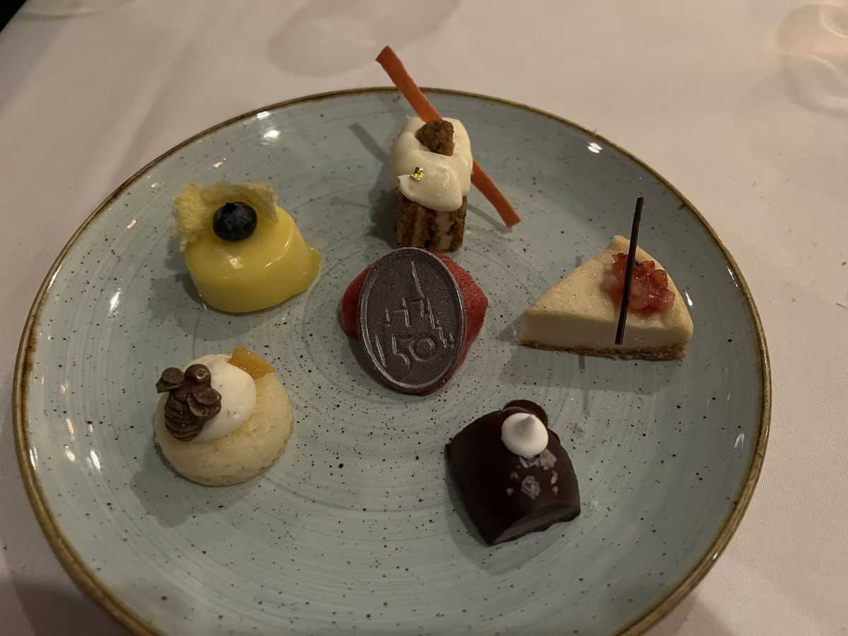 Six assorted mini desserts displayed on a light blue plate, each uniquely topped with fruit, chocolate, or cream—an ideal treat to enjoy alongside one of Disney World’s signature drinks or even the exclusive $137 cocktail, adding an extra sprinkle of magic to your Walt Disney World adventure.