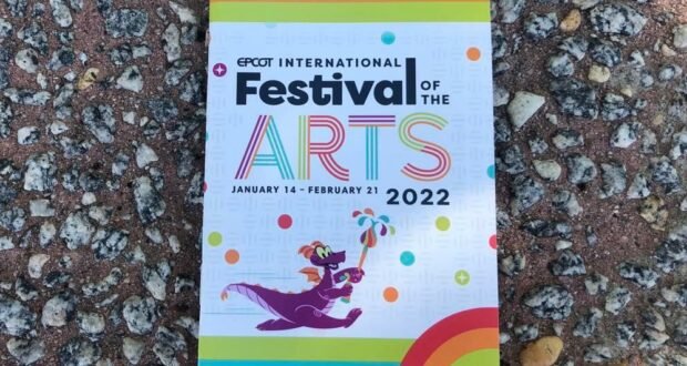 EPCOT International Festival of the Arts 2022 passport resting on gravel, framed by vibrant rainbow borders and featuring Figment holding a paintbrush—capturing the festive energy and creative excitement that kicks off the park’s Culinary Arts celebration on Opening Day.